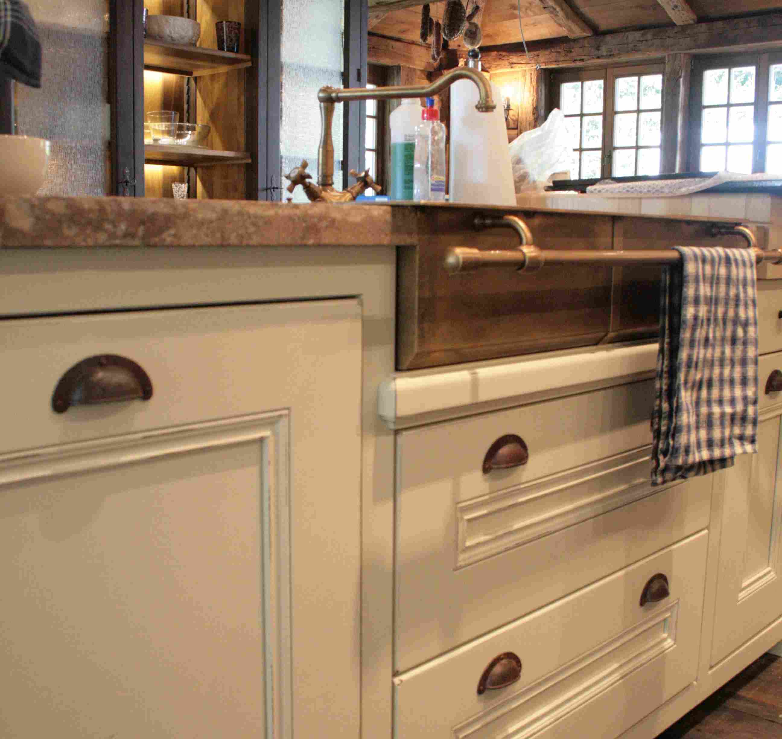 Landhausstil Küche mit cremefarbenen Schubladen, Messingspüle und kariertem Geschirrtuch Detailansicht einer rustikalen Küche im Landhausstil mit cremefarbenen Schubladen, Messingspüle und kariertem Geschirrtuch an der Stange