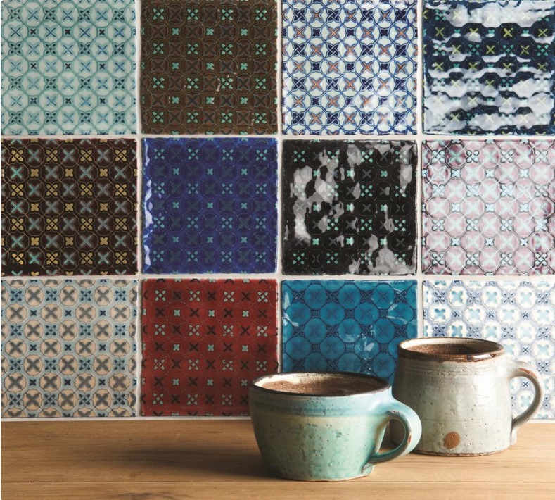 Bunte Fliesenwand mit geometrischen Mustern und zwei Keramiktassen auf Holz Verschiedenfarbige, dekorative Fliesen mit geometrischen Mustern und zwei grüne Keramiktassen auf einer Holzoberfläche