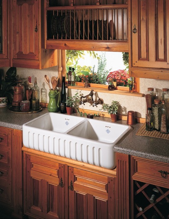 Landhausstil-Küche mit weißem Keramik-Doppelwaschbecken und Holzmöbeln Weiße Keramik-Doppelspüle in einer rustikalen Küche mit Holzmöbeln, Blick aufs Fenster mit Blumen