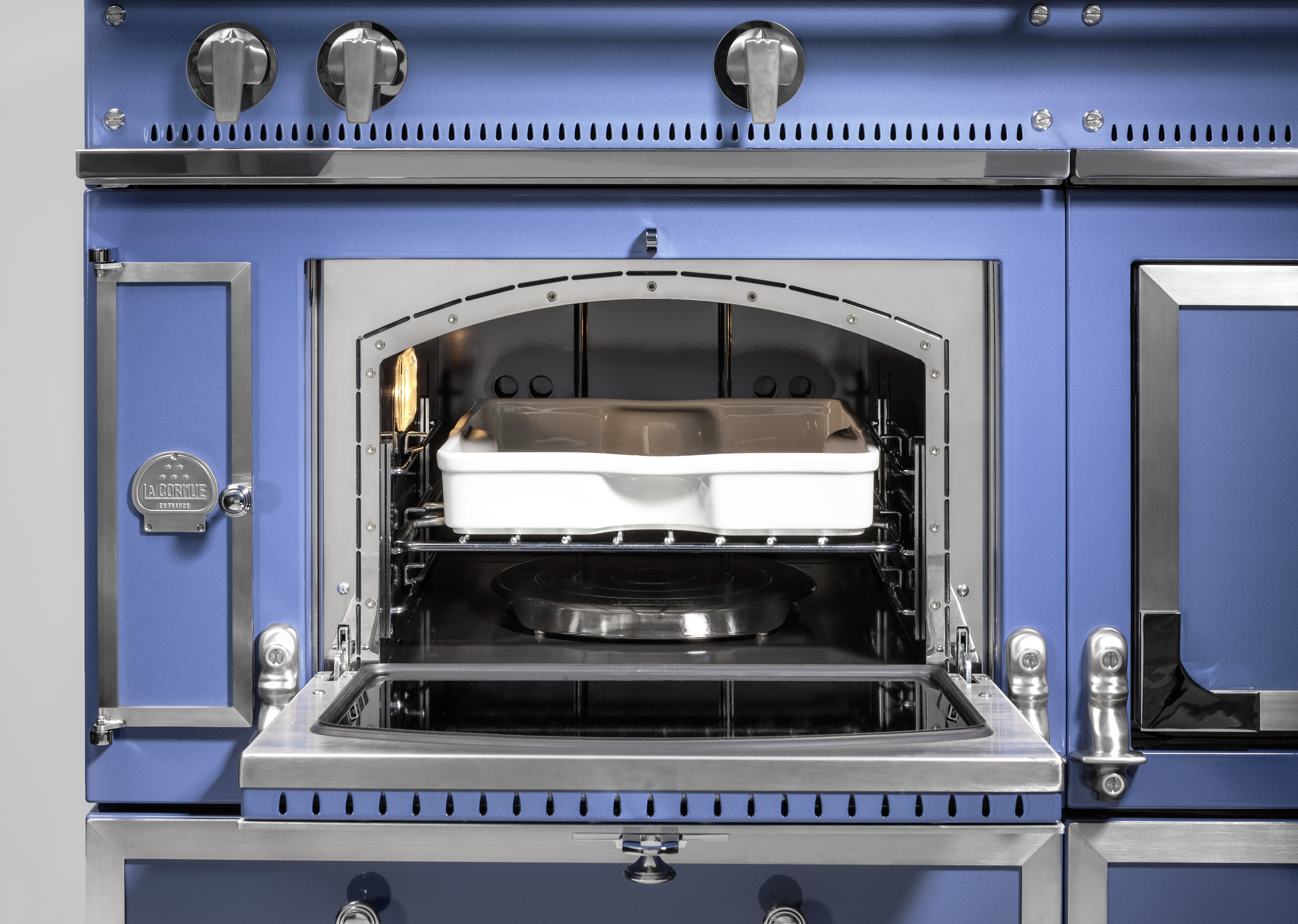 Blauer Backofen mit offener Tür und weißer Auflaufform im Innenraum Detailaufnahme eines blauen Backofens mit geöffneter Tür und einer weißen Auflaufform auf dem Rost