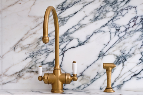 Elegante Küchenarmatur aus Messing mit Marmor-Rückwand, klassisches Design Goldfarbene Küchenarmatur im Retro-Stil mit weißem Griff vor einer Marmorwand, inklusive passendem Spülbrauseaufsatz