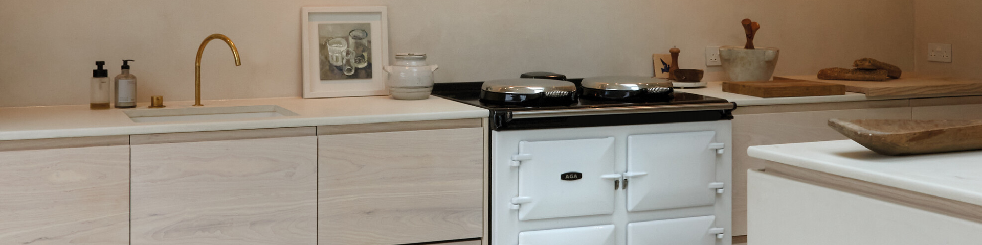 Moderne helle Küche mit weißem AGA-Herd und goldener Armatur Helle, minimalistische Küche mit weißem AGA-Herd, goldfarbener Küchenarmatur und stilvollen Accessoires auf den Arbeitsflächen