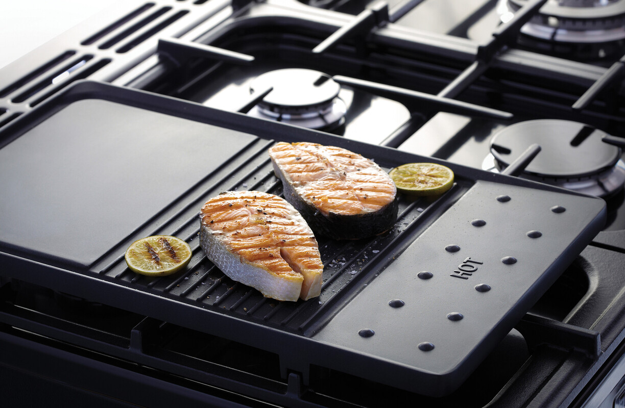 Gusseiserne Grillplatte auf Gasherd mit Rillenfläche; gegrillte Lachssteaks und Limettenscheiben – robuste Plancha für gleichmäßige Hitze und fettarmes Braten