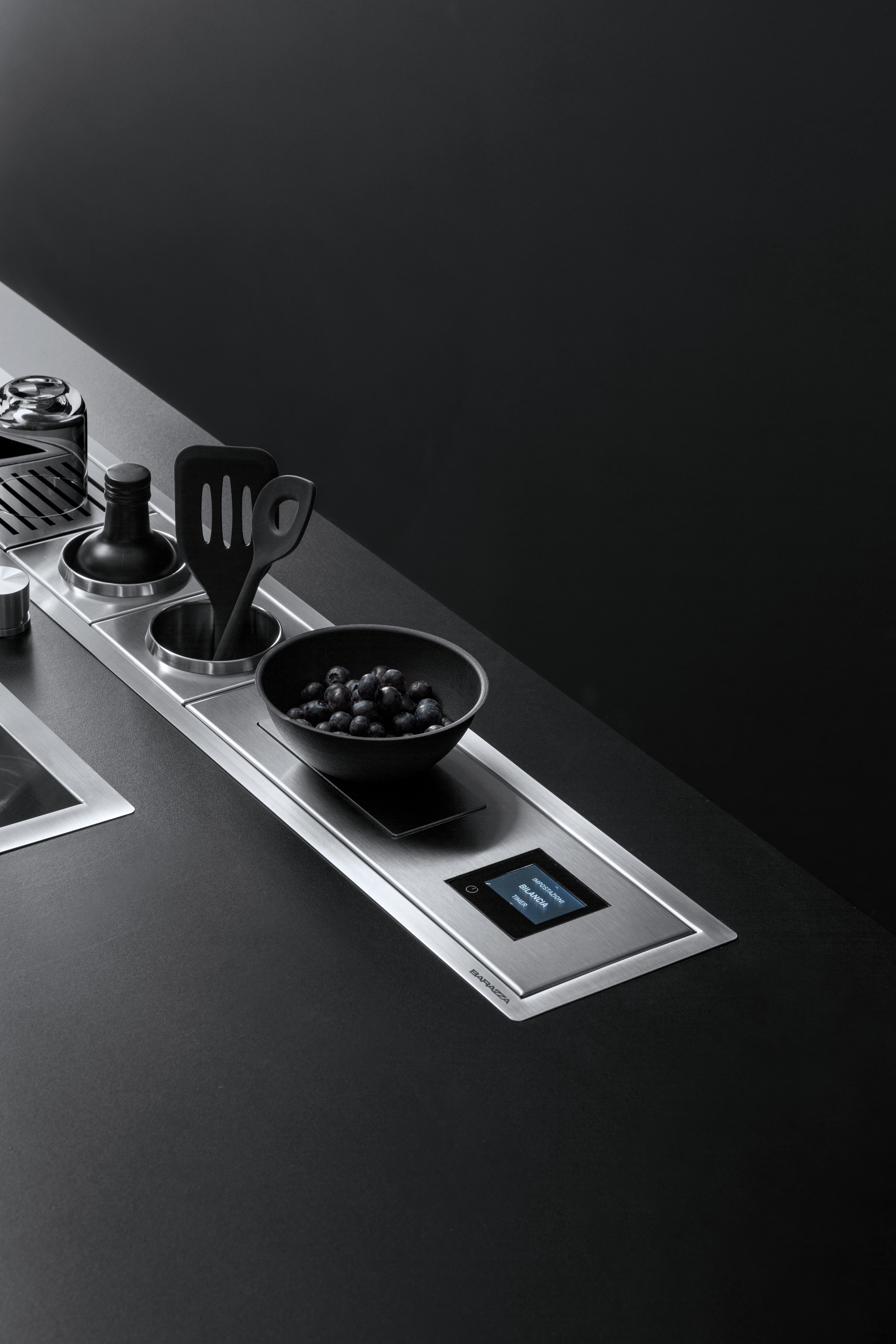 Moderne schwarze Küchenarbeitsplatte mit integriertem Bedienfeld, Schale mit Trauben und Küchenutensilien Elegante Küchenzeile mit eingebautem Touch-Bedienfeld, Schale mit Trauben und Küchenutensilien auf einer schwarzen Arbeitsfläche