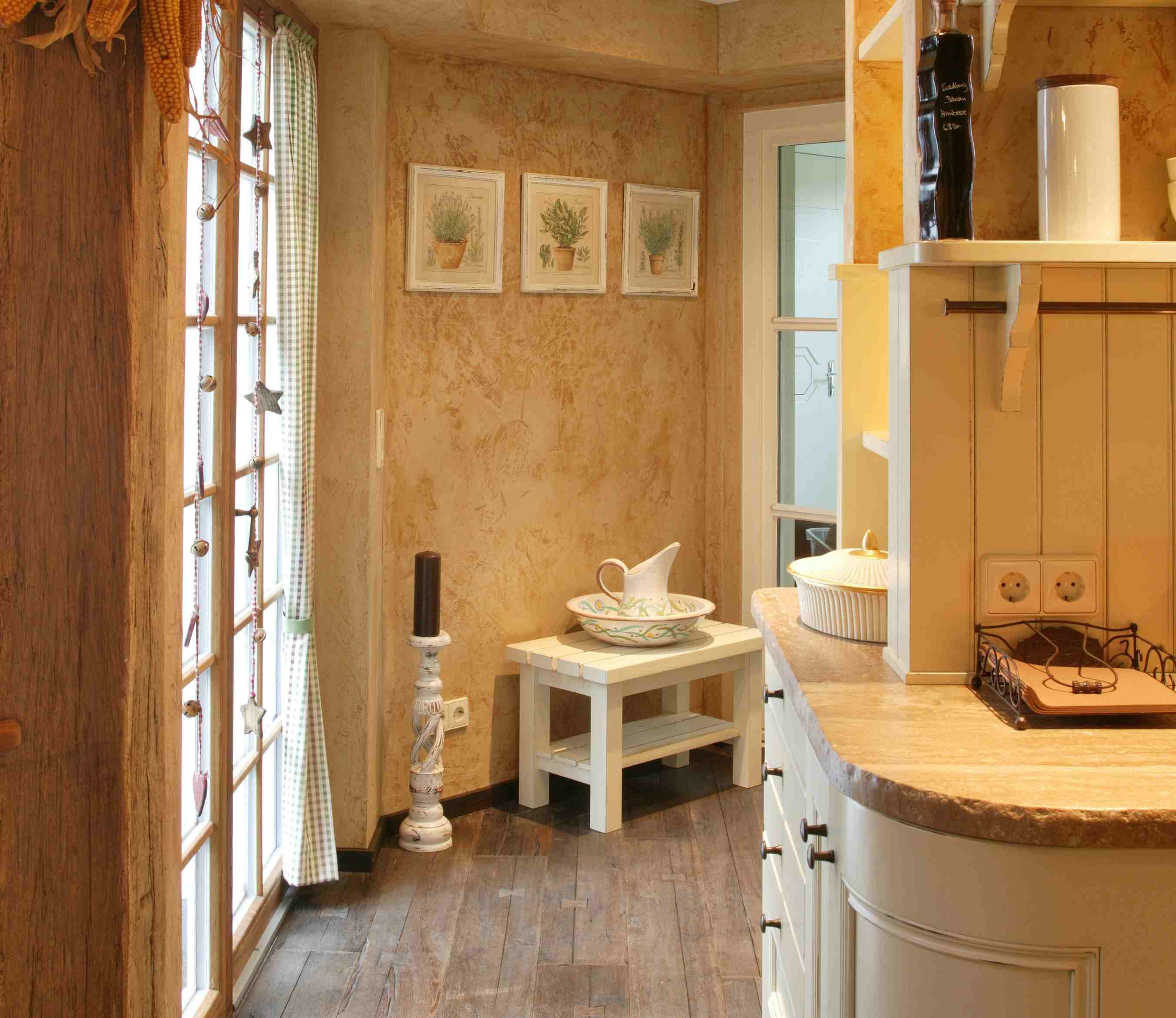 Gemütliche Landhausküche mit rustikalen Holzmöbeln und dekorativen Accessoires Helle Landhausküche mit Holzboden, cremefarbenen Schränken, dekorativen Wandbildern und einem Fenster mit Vorhang im Landhausstil