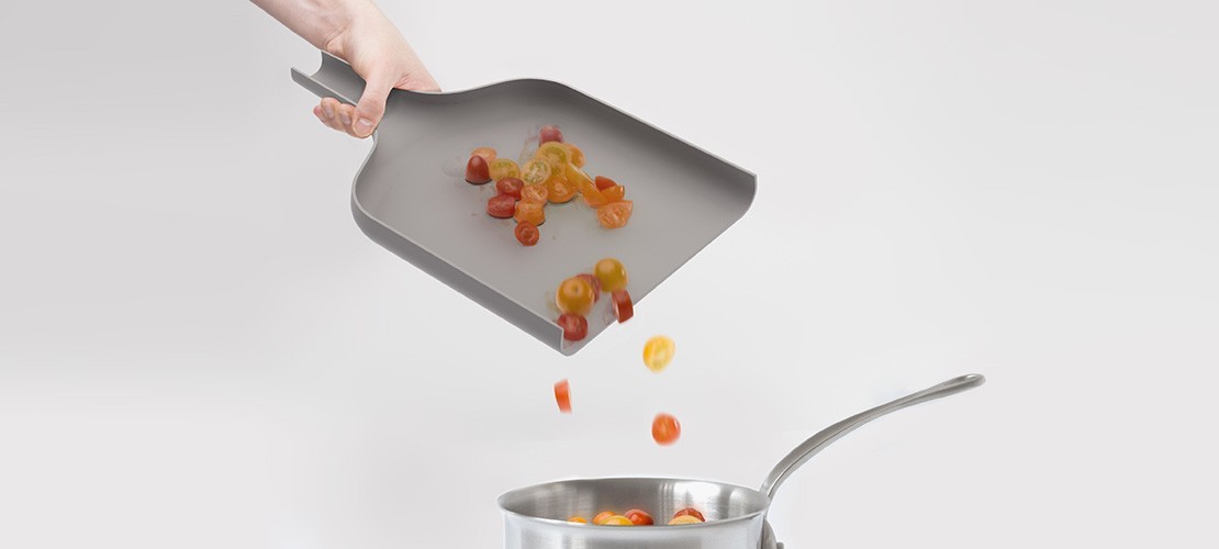 Eine Hand hält eine flexible Küchenhilfe, die Kirschtomaten in einen Topf schüttet.