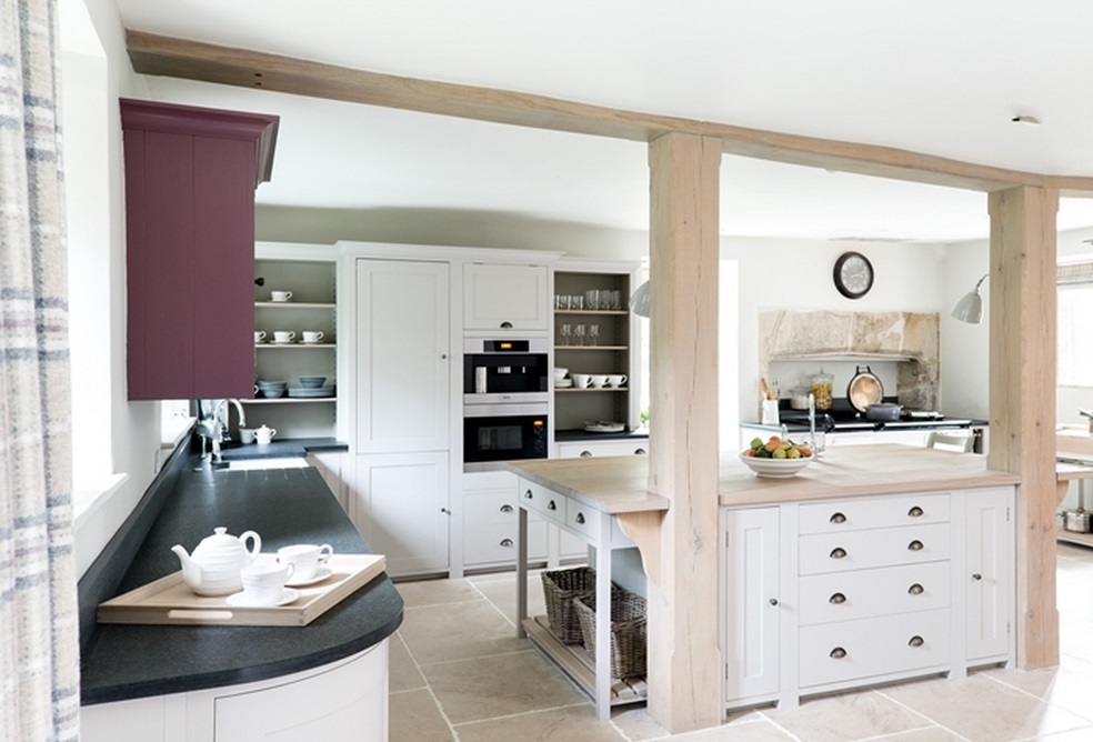 Moderne Landhausküche mit Kochinsel, weißen Schränken und gemütlicher Atmosphäre Große, helle Landhausküche mit weißer Kochinsel, schwarzen Arbeitsplatten, Geschirr auf Tablett und Obstschale auf Holzarbeitsfläche