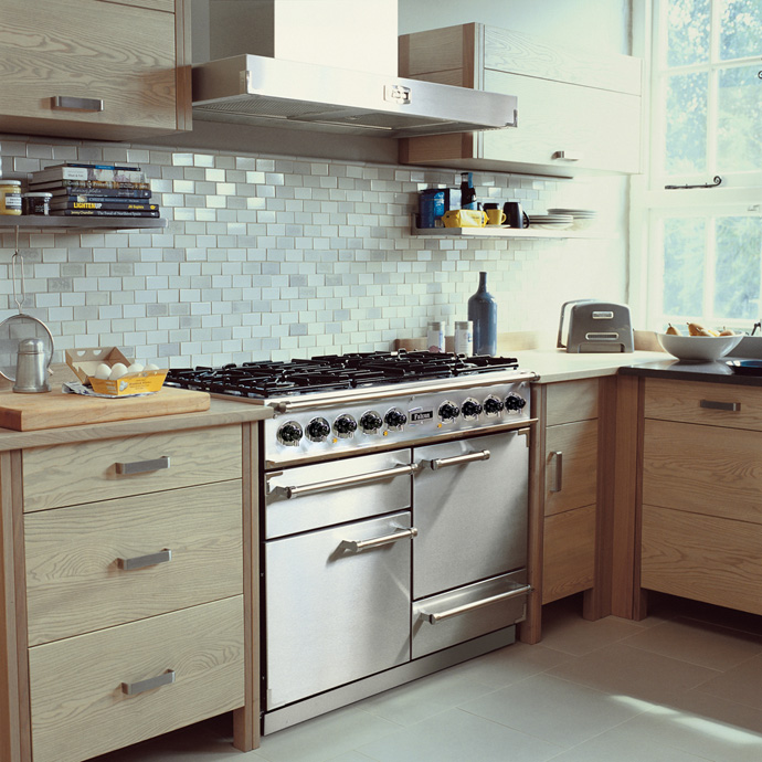 Moderne Edelstahlküche mit großem Gasherd und heller Holzoptik Küche mit Edelstahl-Gasherd, Dunstabzugshaube, hellen Holzschränken und Fliesenspiegel in Weiß