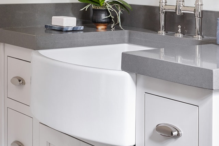 Moderne Küchenspüle mit grauer Arbeitsplatte und Chromarmaturen Weiße Farmhouse-Küchenspüle mit grauer Arbeitsplatte, Chromarmaturen und dekorativer Pflanze