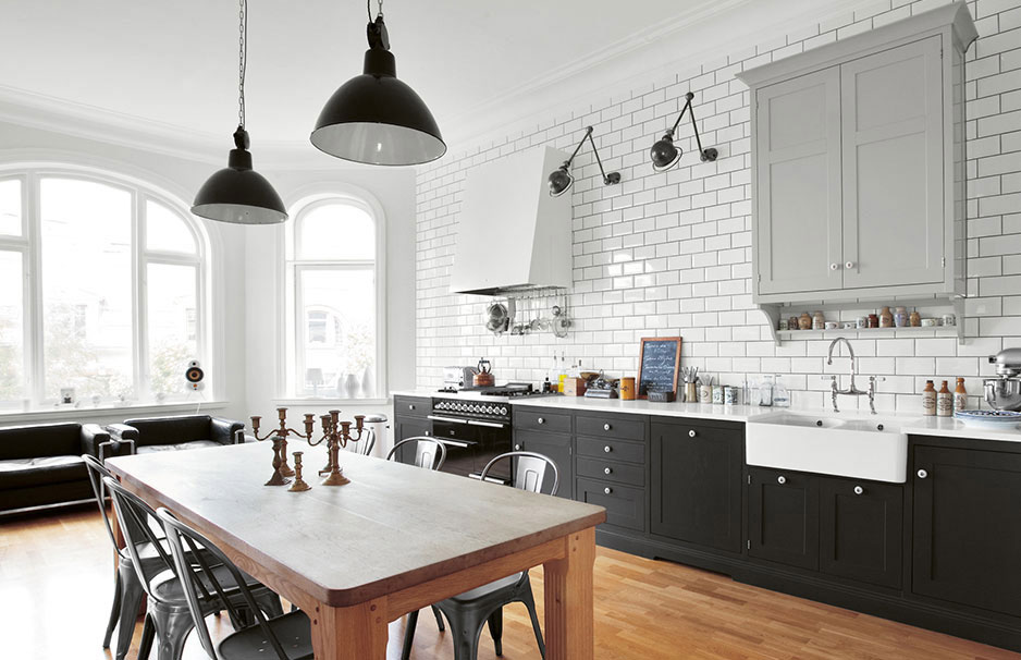 Moderne helle Küche mit Landhausstil und Esstisch aus Holz Helle, moderne Küche im Landhausstil mit weißen Fliesen, dunklen Unterschränken, großem Holzesstisch, Metallstühlen und zwei schwarzen Hängelampen