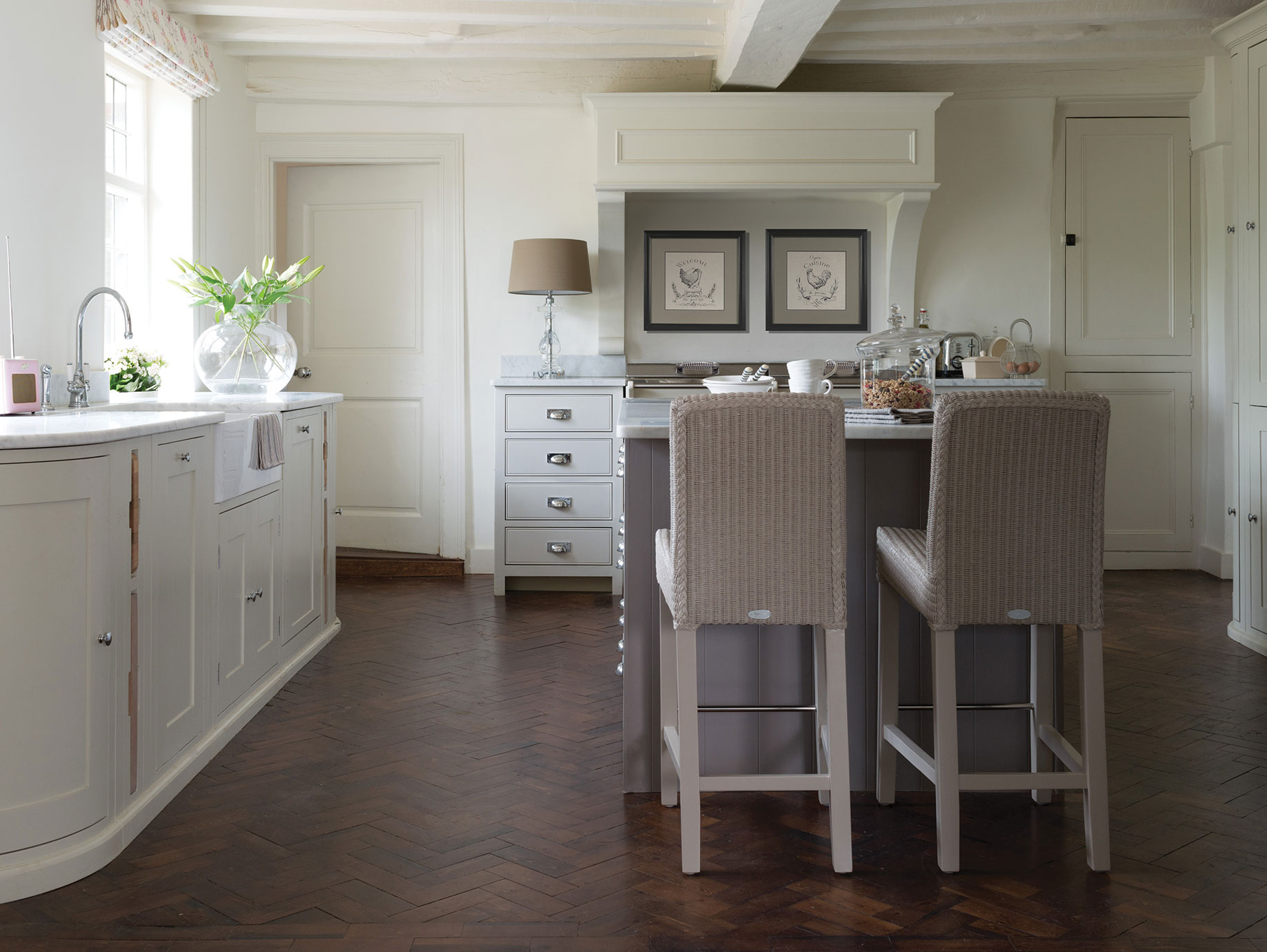 Moderne Landhausküche mit Kücheninsel und Barhockern in heller Farbgestaltung Helle, geräumige Landhausküche mit Kücheninsel, zwei geflochtenen Barhockern, Marmorarbeitsplatten, dekorativen Bildern und Holzboden