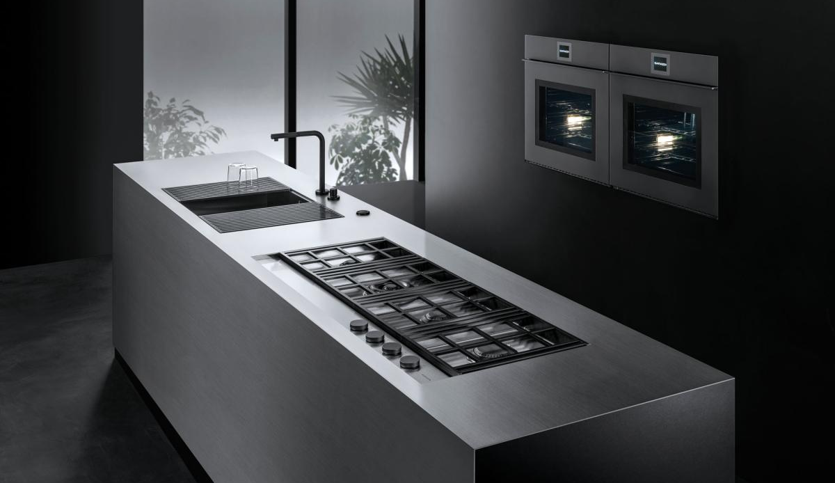 Moderne Designküche mit Edelstahl-Kochinsel, Gasherd, Spüle und zwei Einbaubacköfen Moderne Küche mit Edelstahlinsel, Gasherd, Spüle und zwei schwarzen Einbaubacköfen an der Wand