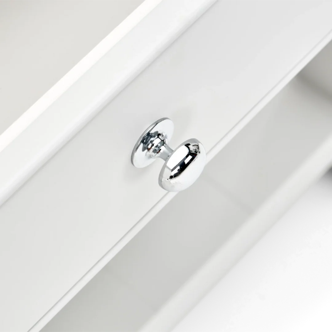 Detailansicht: verchromter Möbelknopf an weißer Schublade; glänzender, runder Griff als Ersatz- oder Beschlagteil für Kommode, Sideboard oder Badschrank