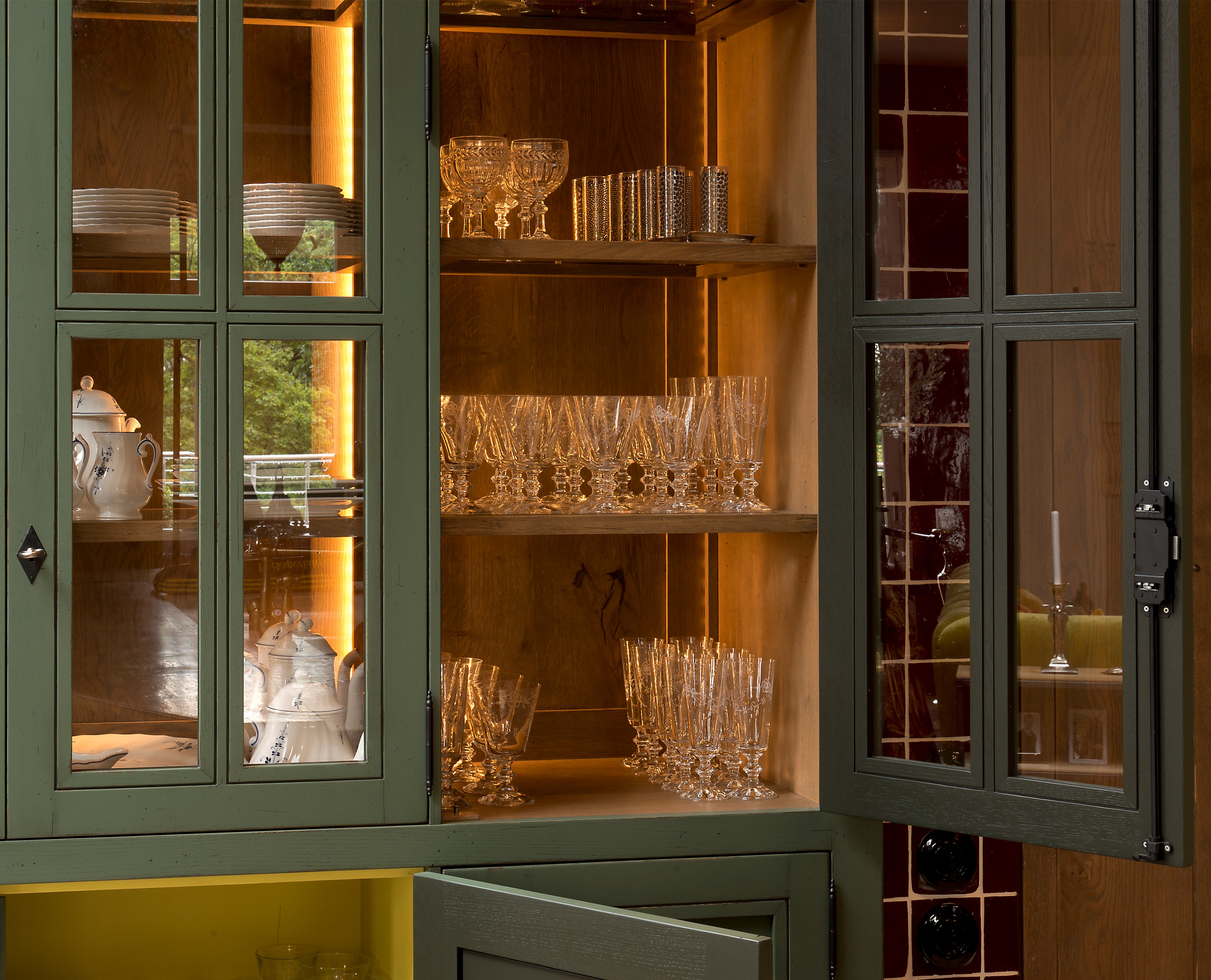 Beleuchteter Vitrinenschrank mit Gläsern, Tassen und Porzellangeschirr Offener, beleuchteter Vitrinenschrank mit Gläsern, Porzellan-Teeservice und Tellern auf Holzregalen
