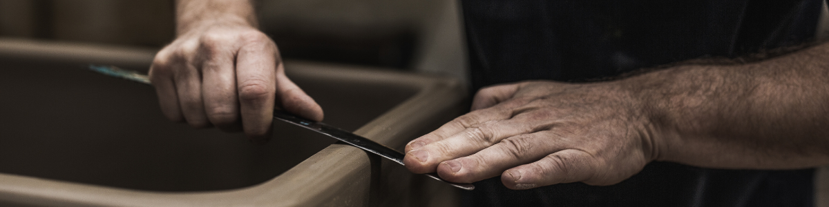 Handwerkliche Bearbeitung von Ton mit einem Werkzeug Nahaufnahme von Händen, die mit einem Werkzeug Ton an der Kante eines Keramikobjekts bearbeiten