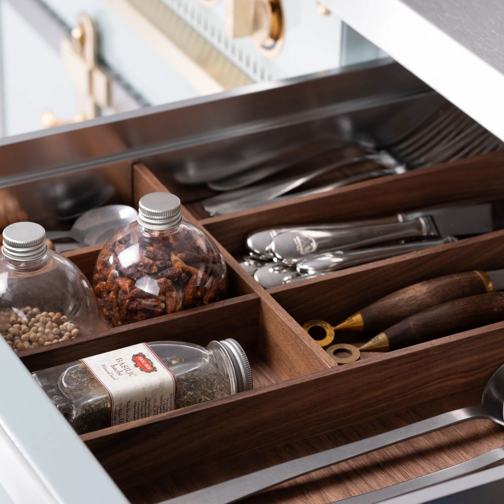 Offene Küchenschublade mit hochwertigem Nussbaum-Besteckkasten; sauber sortierte Löffel, Gabeln, Messer und Gewürzgläser – praktischer Organizer für Ordnung in der Küche