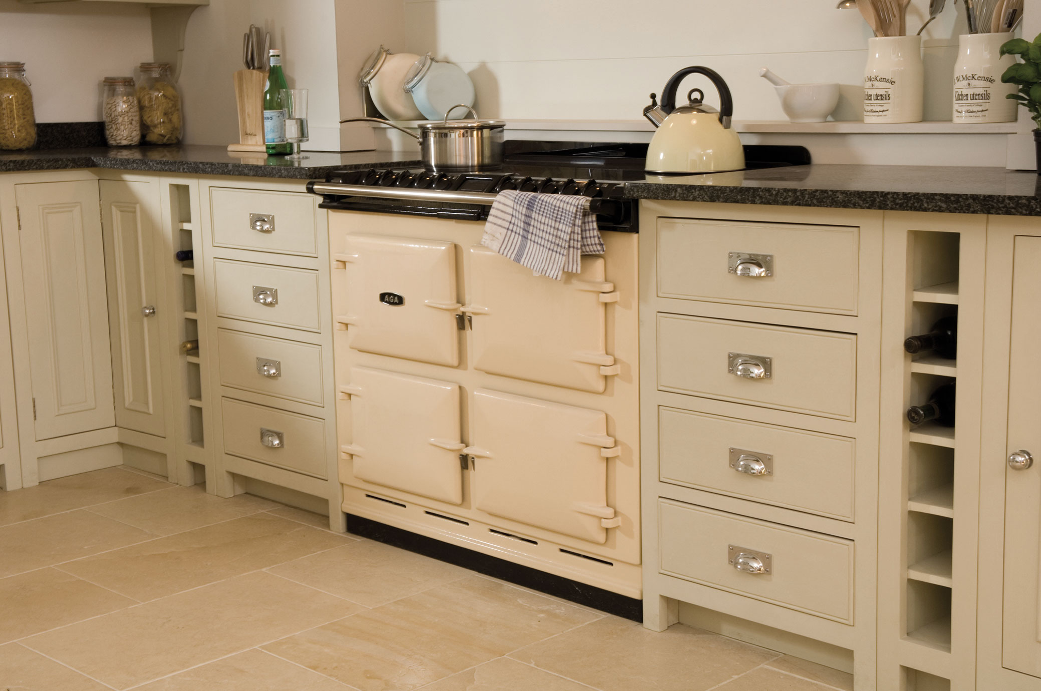 Klassischer cremefarbener AGA-Küchenherd in stilvoller Landhausküche Cremefarbener AGA-Küchenherd mit vier Ofenklappen, umgeben von hellen Landhaus-Küchenschränken, Utensilien und Vorratsgläsern