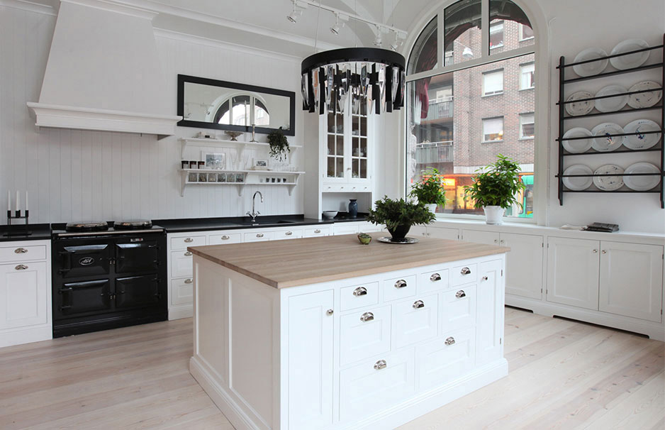 Moderne, helle Landhausküche mit Kücheninsel und großen Fenstern Helle Küche im Landhausstil mit weißer Kücheninsel, Holzarbeitsplatte, schwarzen Akzenten, großem Fenster und dekorativen Pflanzen