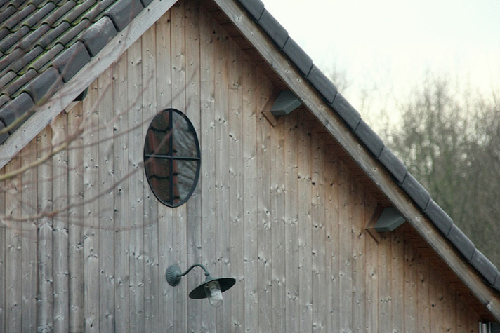Außenansicht eines Holzhaus-Giebels mit rundem Fenster und Außenleuchte Giebel eines Hauses aus Holz mit rundem Fenster und einer schwarzen Außenlampe darunter