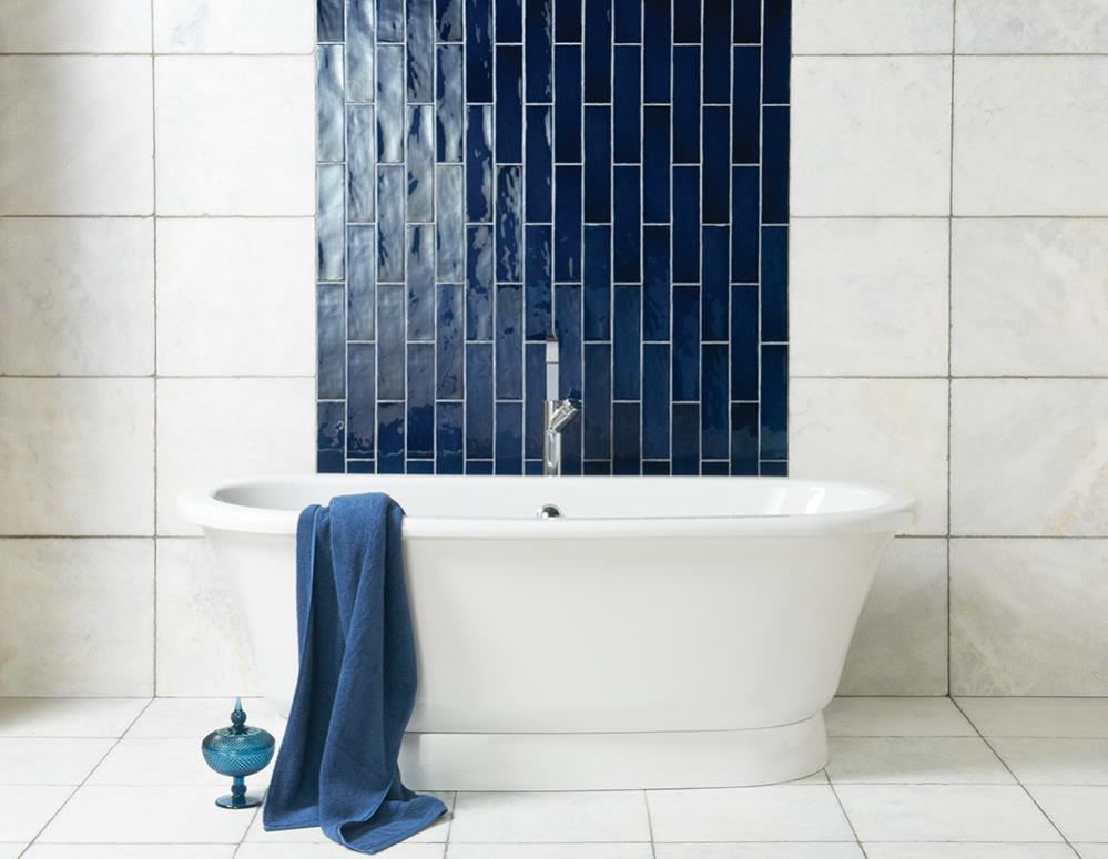 Freistehende Badewanne mit dunkelblauer Akzentfliese und Handtuch – modernes Badezimmerdesign Weiße freistehende Badewanne vor Wand mit dunkelblauen Fliesen, davor ein blaues Handtuch und Dekovase auf Fliesenboden