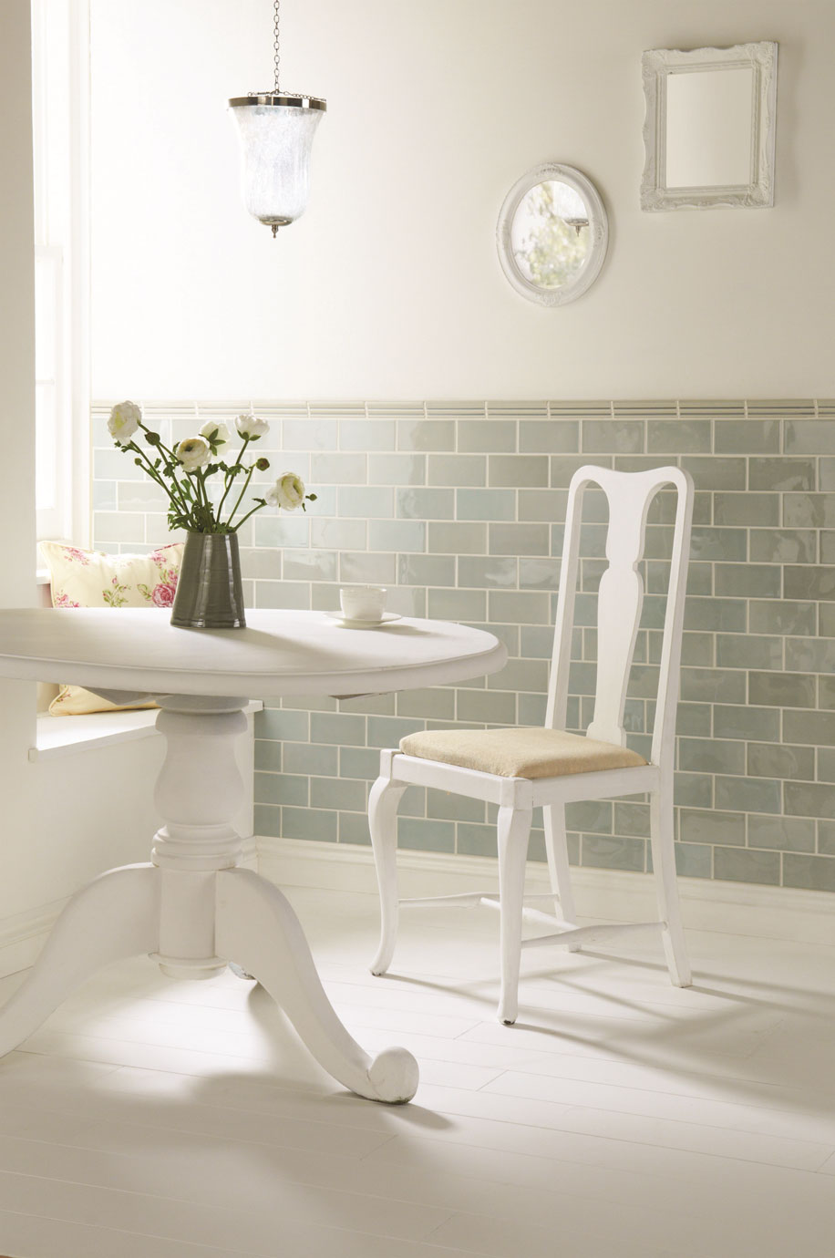 Heller Essbereich mit weißem Tisch, klassischem Stuhl und blauen Wandfliesen im Landhausstil Heller, gemütlicher Essbereich mit weißem Tisch, klassischem Stuhl mit Polster, Vase mit Blumen, hellblauen Kacheln an der Wand und stilvoller Dekoration