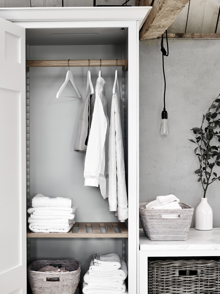 Offener Kleiderschrank mit Hängefächern, gefalteten Handtüchern und geflochtenen Körben in modernem, skandinavischem Design Offener Kleiderschrank mit weißen Hemden auf Bügeln, gefalteten Handtüchern und geflochtenen Aufbewahrungskörben aus natürlichem Material.