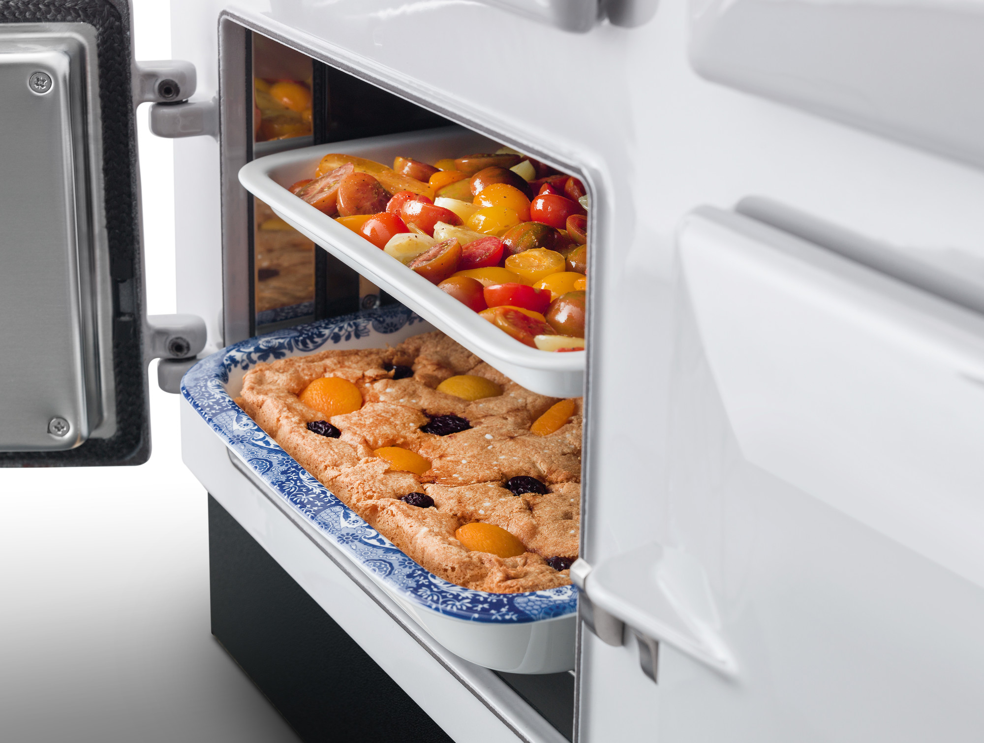 Leckere Auflaufformen mit frischem Obstkuchen und Ofengemüse im Backofen Zwei Auflaufformen im geöffneten Backofen, oben buntes Ofengemüse, unten ein Obstkuchen mit Aprikosen und Kirschen