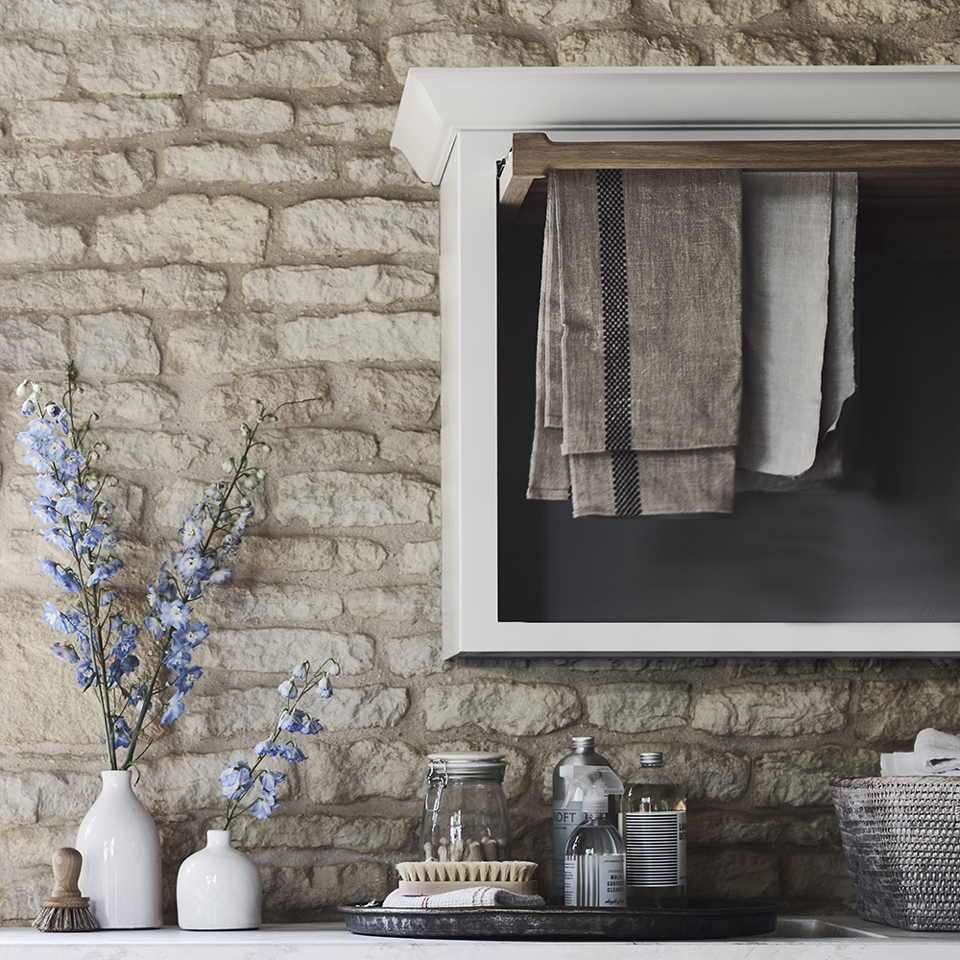 Modernes Küchenregal mit Geschirrtüchern, Vasen mit Blumen und Vorratsgläsern vor Steinwand Hell eingerichtete Küchenszene mit Steinwand, weißen Vasen mit blauen Blumen, Ablage mit Geschirrtüchern, Gläsern und Reinigungsutensilien
