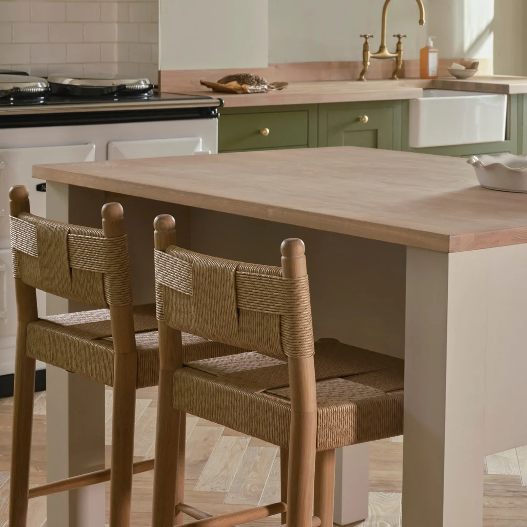 Zwei Barhocker aus Holz mit handgeflochtener Sitz- und Rückenlehne an einer Kücheninsel aus Holz; ideal als Tresenhocker für Landhausküchen.