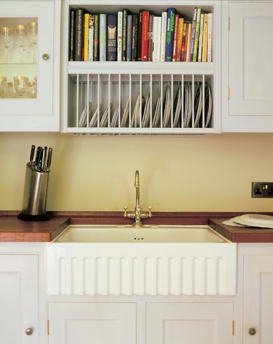 Küchenspüle mit Keramikbecken, Geschirrablage und Bücherregal oberhalb, klassische Landhausküche Landhausküche mit weißem Keramikspülbecken, darüber ein Regal mit Geschirr und Kochbüchern, Messerblock auf der Arbeitsplatte