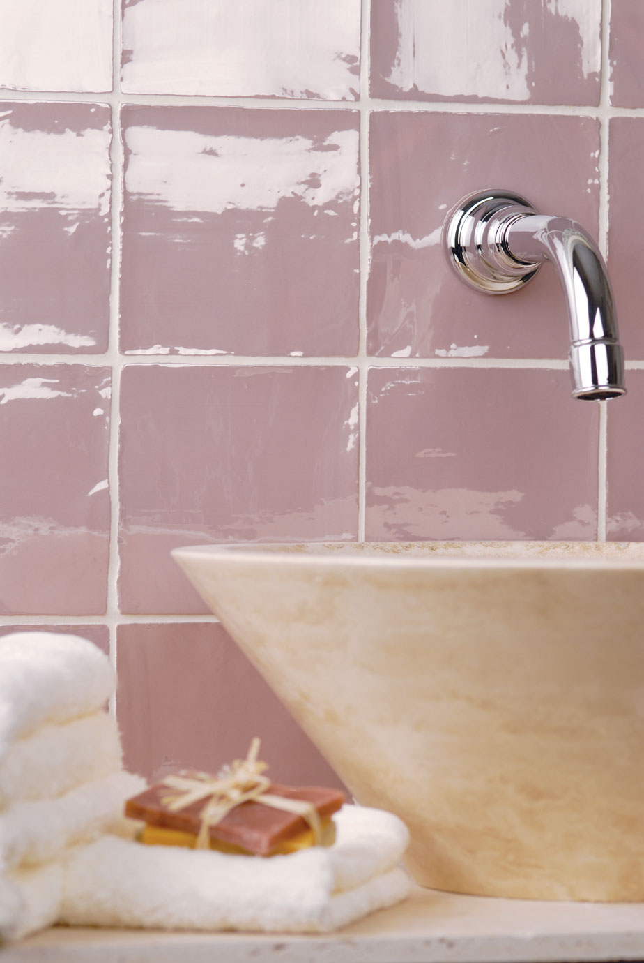 Waschbecken mit moderner Wandarmatur vor rosa Wandfliesen im Badezimmer Moderner Badezimmerbereich mit cremefarbenem Waschbecken, Wandarmatur aus Chrom, rosa Wandfliesen, weißen Handtüchern und Seife