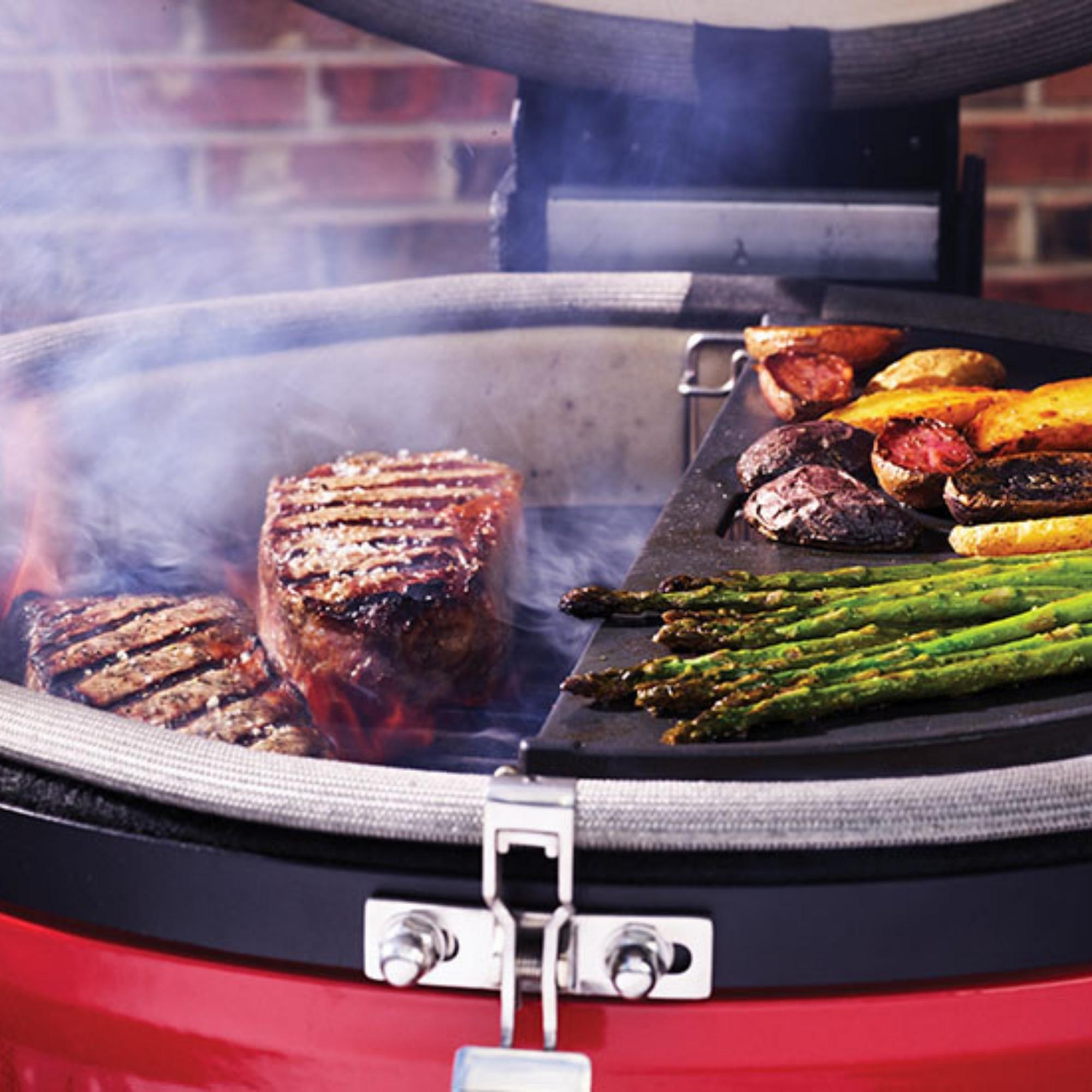 Grill mit saftigen Steaks, grünem Spargel und Kartoffeln auf einer Grillplatte – leckeres Barbecue-Erlebnis Saftige Steaks, grüner Spargel und Kartoffeln werden nebeneinander auf einem modernen Grill mit Grillplatte zubereitet, im Hintergrund ist Rauch zu sehen.