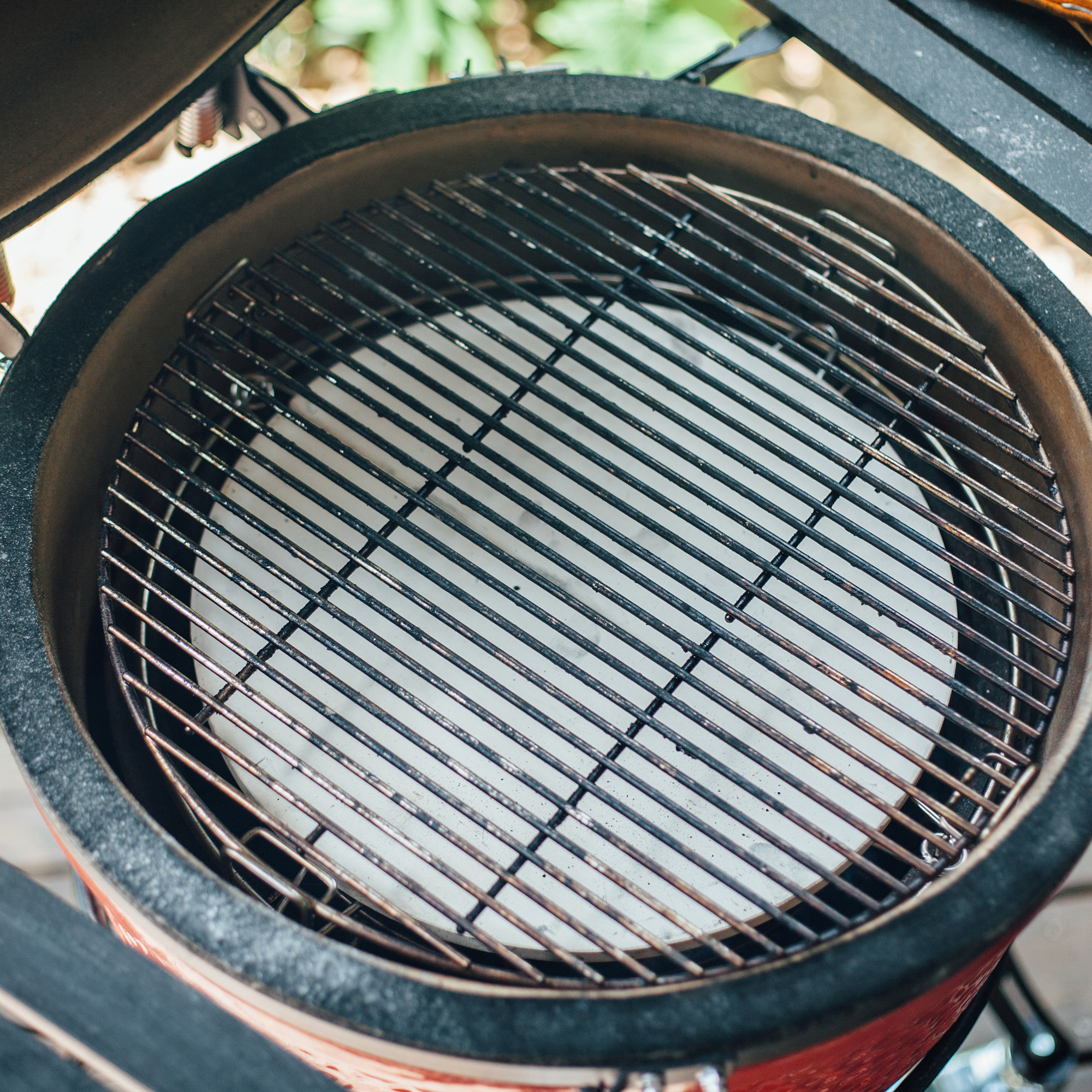 Keramikgrill mit hitzebeständigem Grillrost und Pizzastein für indirektes Grillen Offener Keramikgrill mit Metall-Grillrost und rundem Pizzastein, ideal für indirektes Grillen und Backen im Garten