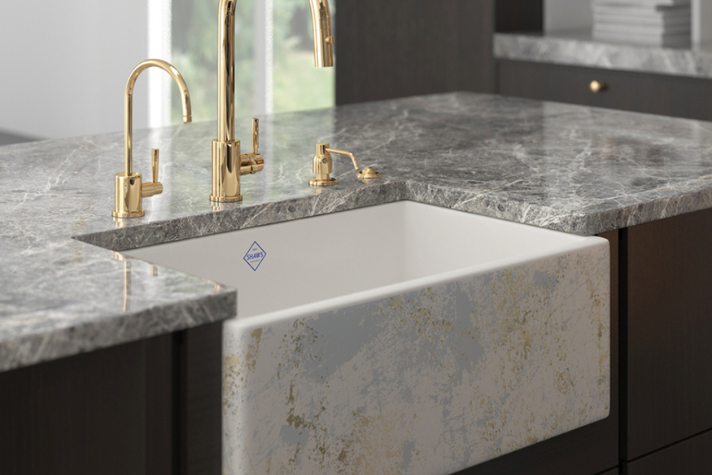 Moderne Küchenspüle aus Keramik mit goldenen Armaturen und grauer Marmorarbeitsplatte Hochwertige weiße Keramikspüle mit einzigartigem Muster, goldfarbenen Wasserhähnen und eleganter Arbeitsplatte aus grauem Marmor in einer modernen Küche