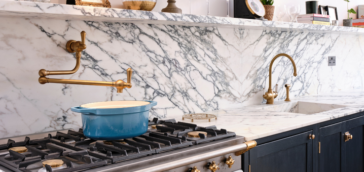 Moderne Küche mit Marmorarbeitsplatte, goldenen Armaturen und Gasherd Stilvolle Küche mit Marmorarbeitsplatte, blauem Kochtopf auf dem Gasherd und goldfarbenen Wasserhähnen