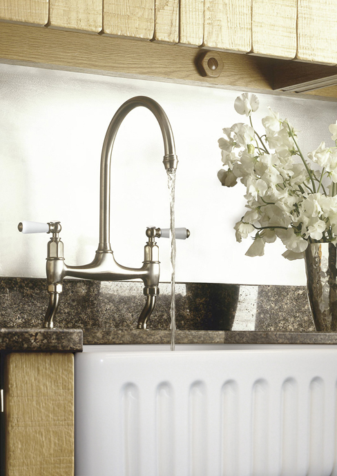 Elegante Küchenarmatur aus Edelstahl mit Porzellangriffen an weißer Keramikspüle und Blumenvase Nahaufnahme einer modernen Küchenarmatur mit Wasserstrahl über einer weißen Keramikspüle und einem Blumenarrangement auf der Arbeitsplatte