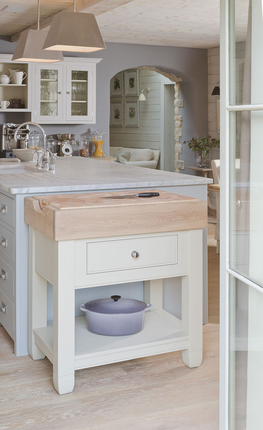 Kücheninsel mit Schneidebrett und Schublade im Landhausstil Helle Kücheninsel mit massivem Holz-Schneidebrett, Schublade und Ablage, darunter ein lila Bräter in einer modernen Landhausküche