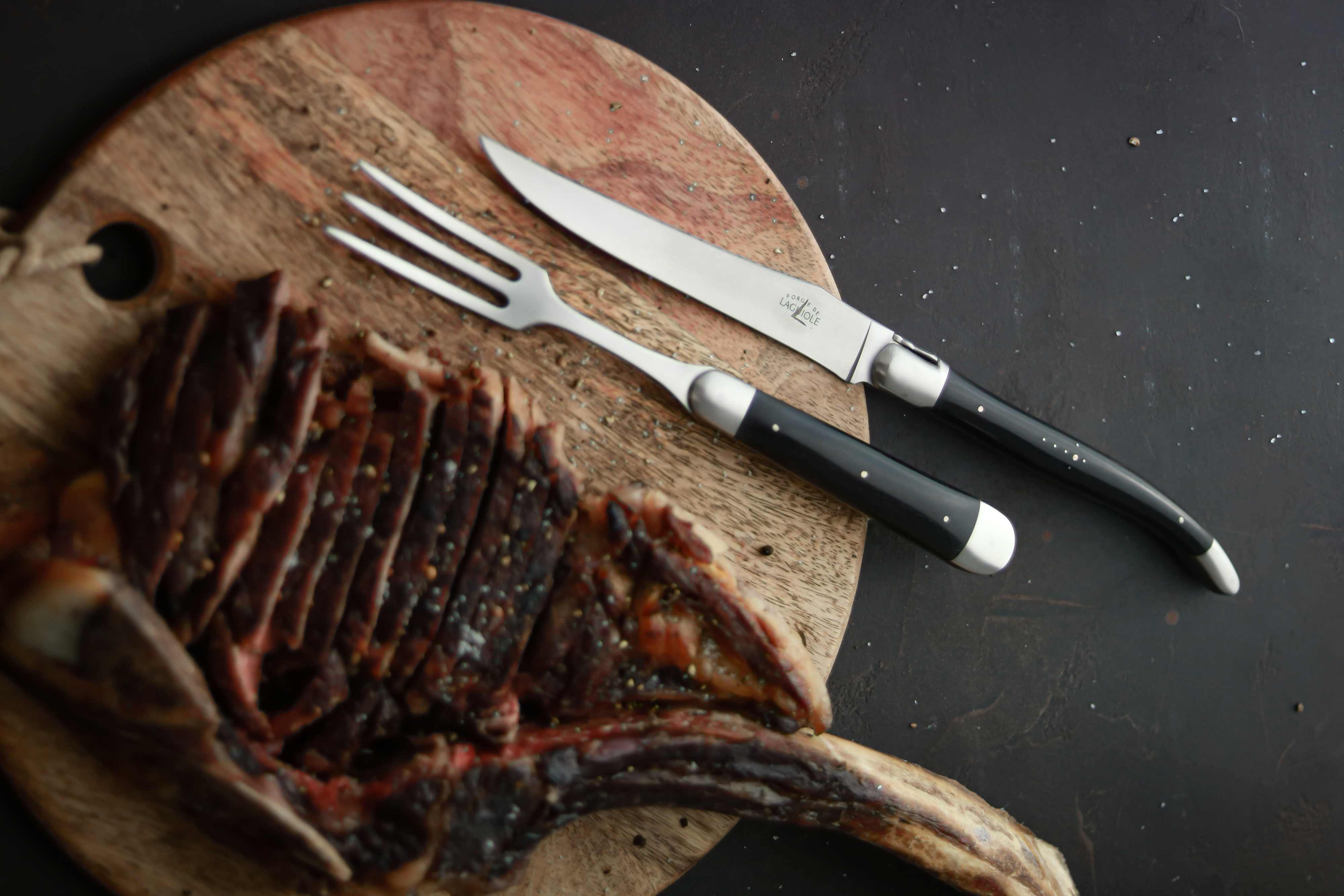 Tranchiergabel und Messer auf Holzbrett neben geschnittenem Steak