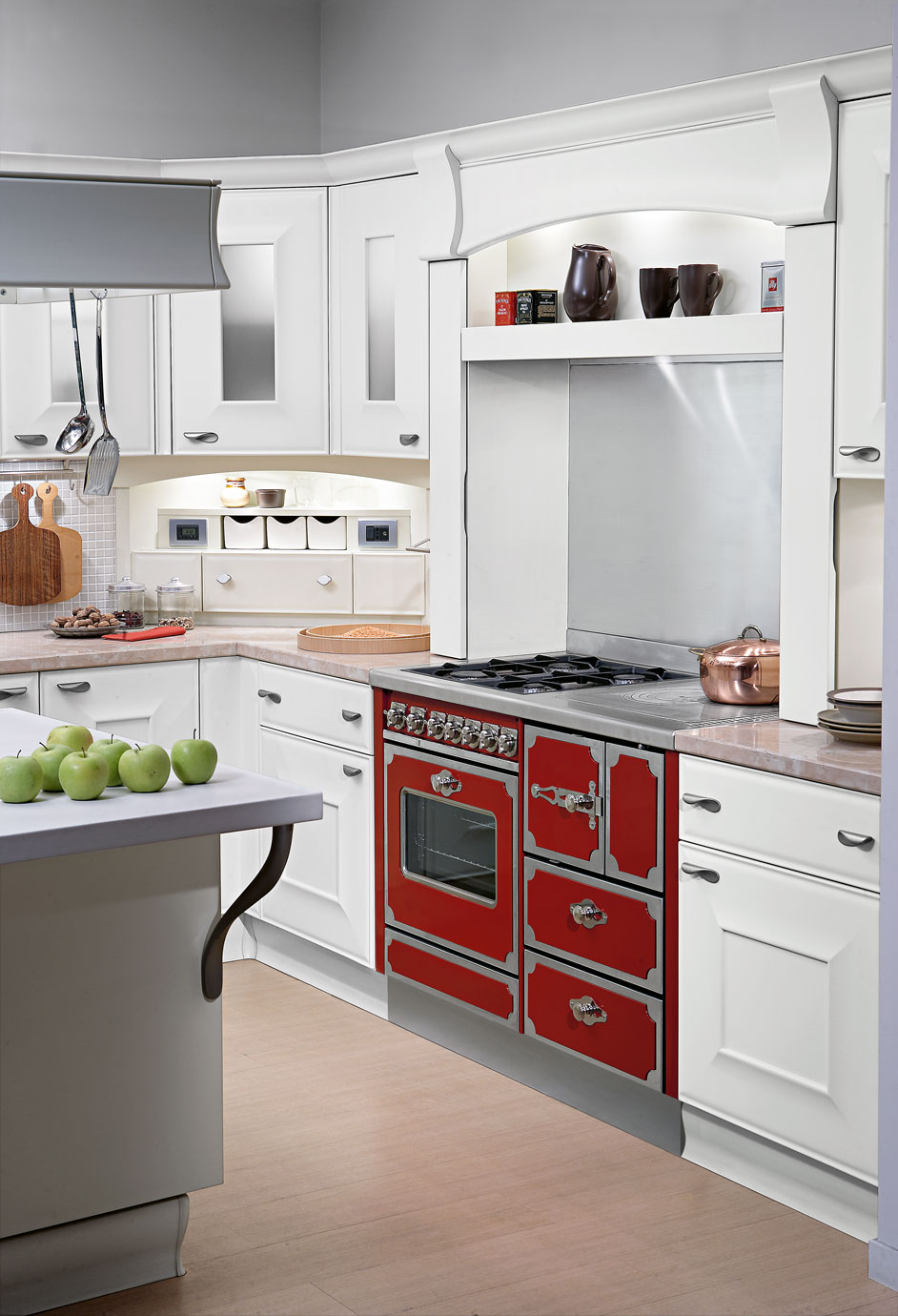 Moderne Landhausküche mit weißer Einrichtung und rotem Retro-Standherd Weiße Einbauküche mit rotem Vintage-Gasherd, hellen Arbeitsflächen und Küchendekoration, darunter grüne Äpfel auf der Kücheninsel