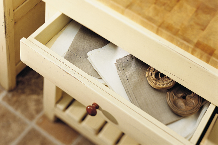 Offene Schublade eines hellen Holzmöbels mit Leinentüchern und Holzdekorationen Detailansicht einer geöffneten Schublade mit gefalteten Leinenservietten und dekorativen Holzornamenten in einem hellen Küchenmöbel.