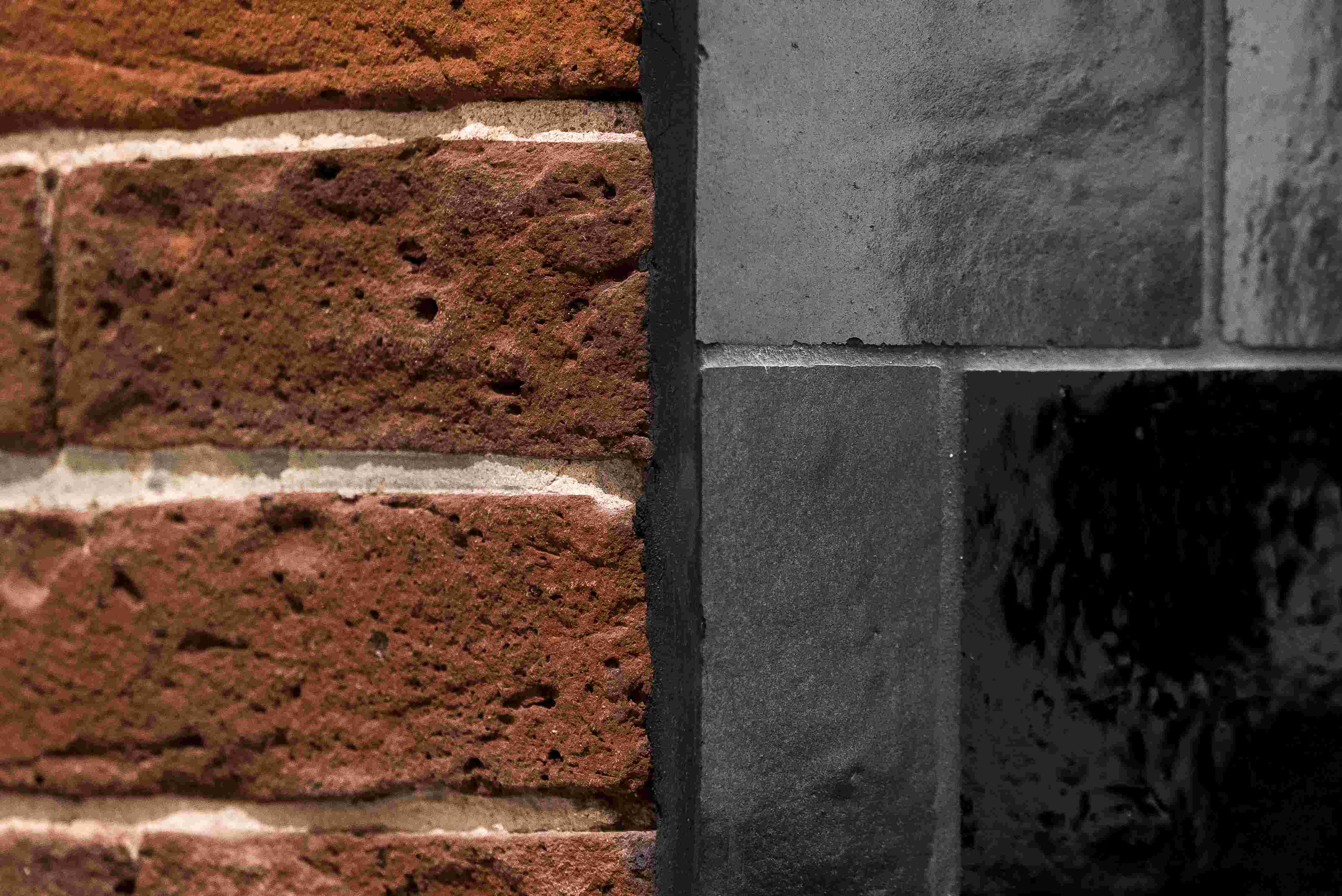 Detailansicht einer roten Backsteinwand neben einer dunkelgrauen Fliesenwand