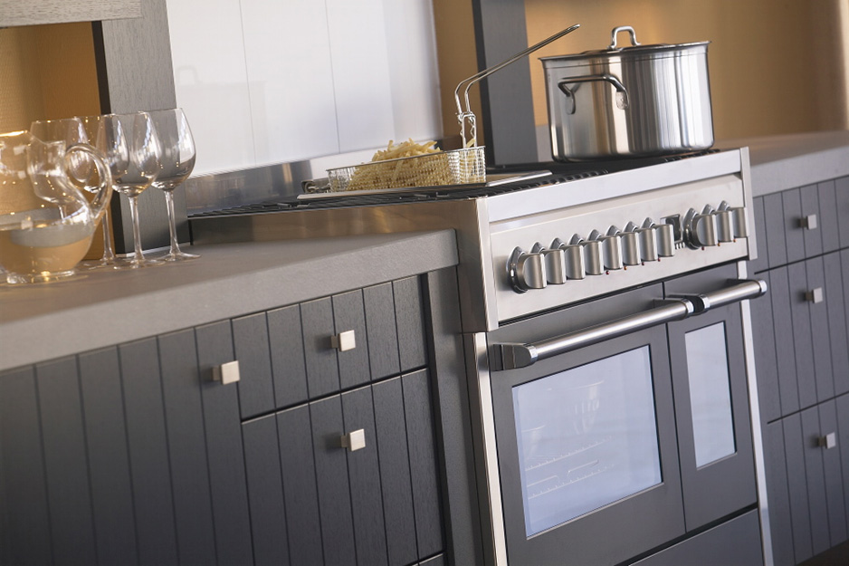Moderne Edelstahl-Küchenzeile mit Backofen, Kochtopf und Frittierkorb auf dem Herd Herd mit Edelstahl-Backofen, Kochtopf und Frittierkorb sowie Weingläsern auf einer eleganten Arbeitsplatte