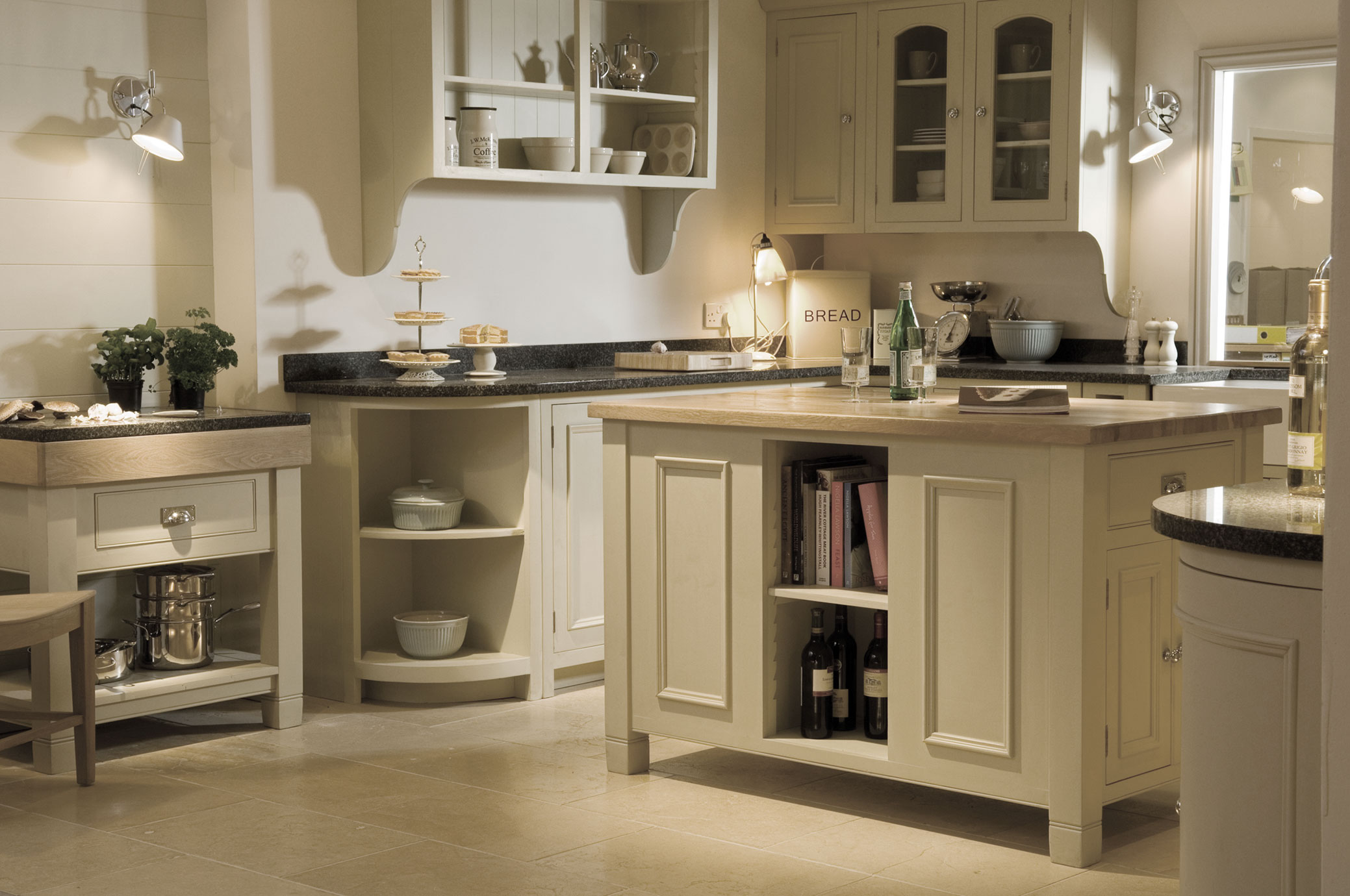 Moderne Landhausküche mit Kücheninsel, helle Fronten und Arbeitsplatten aus Holz und Granit Helle Landhausküche mit Kücheninsel, offenen Regalen, Glasflaschen, Kochbüchern, dekorativen Schalen und modernen Lampen