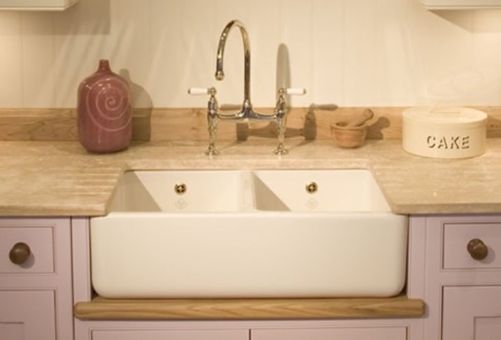 Doppelspülbecken aus Keramik mit klassischem Wasserhahn in einer Landhausküche Keramik-Doppelspülbecken mit goldenen Armaturen, Marmorarbeitsplatte und Küchenaccessoires in Landhausstil