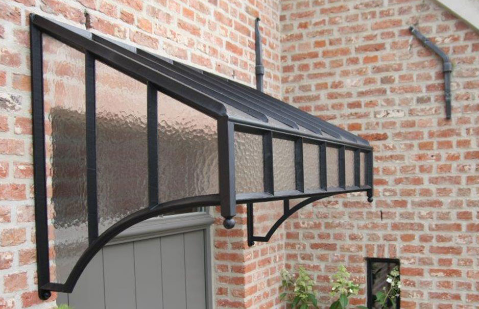 Hochwertiges Vordach aus Glas und Metall für den Hauseingang, modernes Design Vordach aus Glas mit schwarzem Metallrahmen über einer Eingangstür an einer Hausfassade aus rotem Klinker