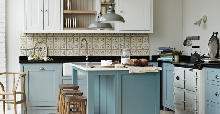 Landhausküche mit hellblauen Schränken, Kücheninsel und dekorativen Fliesen Gemütliche Landhausküche mit hellblauen Unterschränken, weißer Kücheninsel, gemusterten Wandfliesen, Holzhockern und modernem Herd