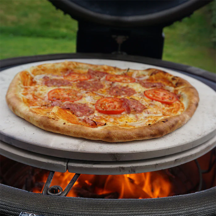 Frisch gebackene Pizza auf einem Pizzastein im Grillofen Hausgemachte Pizza mit Tomaten und Salami auf einem Pizzastein im Grill über Holzfeuer gebacken