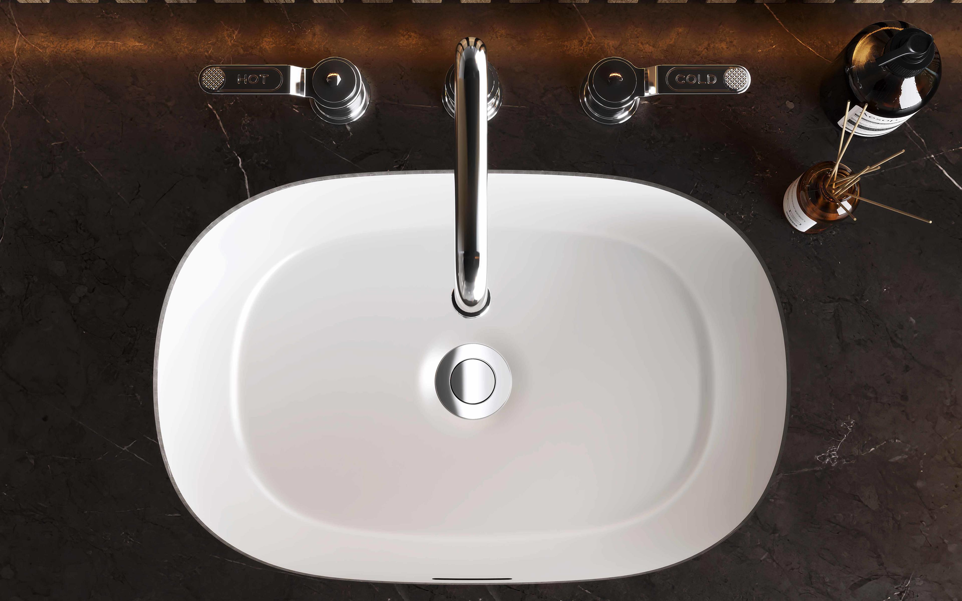 Ovales Keramik-Waschbecken von oben, Chrom-Armatur mit HOT/COLD-Bedienhebeln auf dunkler Marmorplatte, daneben Seifenspender – modernes Bad-Design