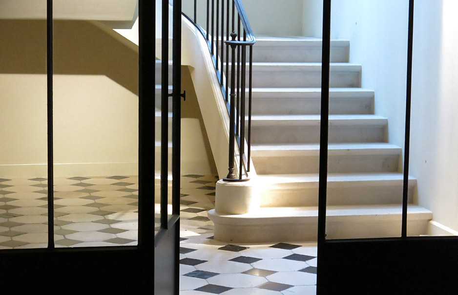 Elegante Steintreppe mit schwarzem Geländer und Schachbrett-Bodenfliesen in modernem Gebäude Innenansicht eines Eingangsbereichs mit weißer Steintreppe, schwarzem Metallgeländer und schwarz-weiß gemusterten Fliesen