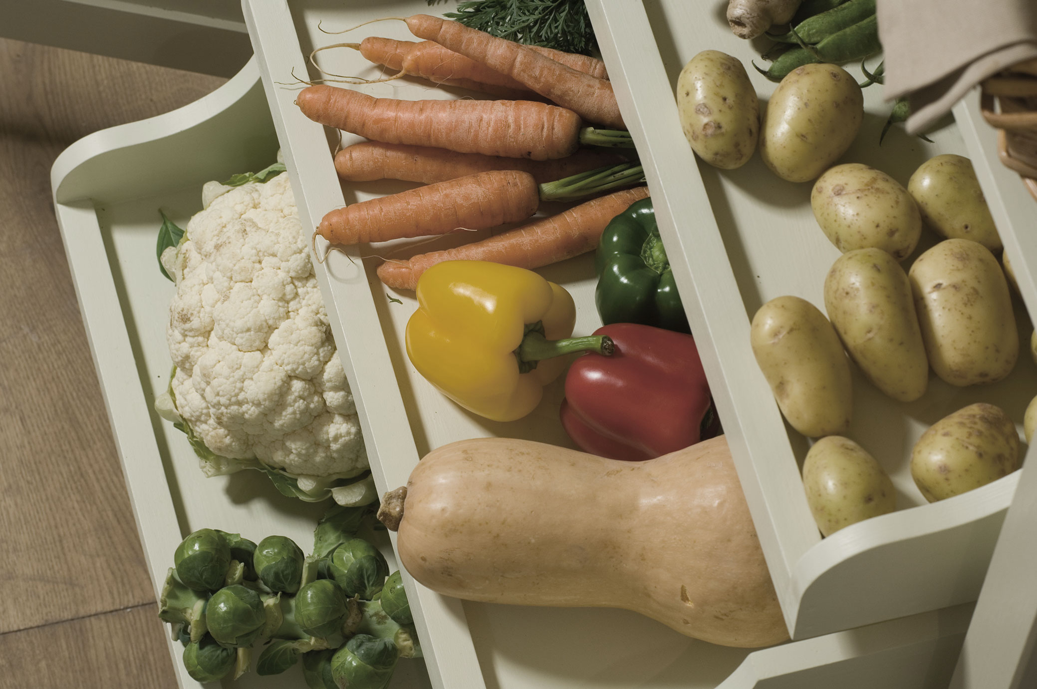 Frisches Gemüse in der Vorratskammer – Kartoffeln, Karotten, Paprika, Blumenkohl und mehr Verschiedene frische Gemüsesorten wie Kartoffeln, Karotten, Paprika, Blumenkohl, Rosenkohl und Butternusskürbis in einem weißen Regal angeordnet